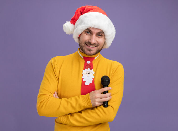 白种人微笑的白人年轻人戴着圣诞帽 打着领带 站在紫色的墙上 站着 拿着麦克风 看起来很孤立 留着复印空间领带抱着封闭