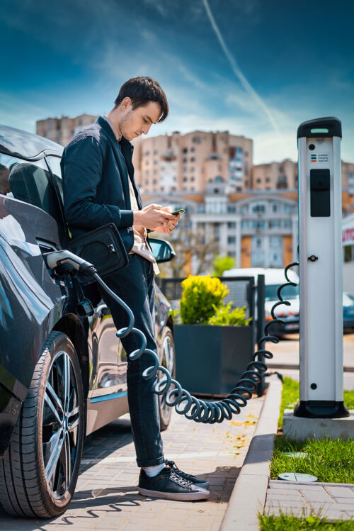未来男人在充电站给他的电动车充电 用智能手机汽车能源交通