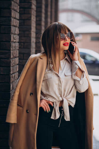 配饰穿米色外套的年轻女子在街上打电话商务女性服装时尚