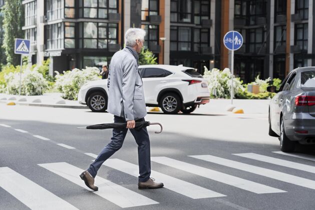老年人时髦的老男人在城市里一边撑着伞过马路成熟老年人雨伞