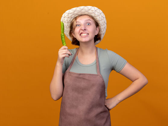帽子恼怒的年轻斯拉夫女园丁戴着园艺帽拿着碎辣椒穿橘子拿着