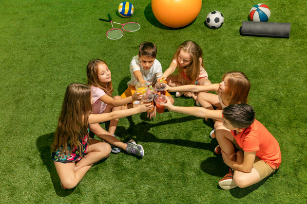 女孩儿童时尚概念一群十几岁的男孩和女孩坐在公园的绿色草地上儿童多彩的衣服 生活方式 流行的色彩概念坐着休闲男孩