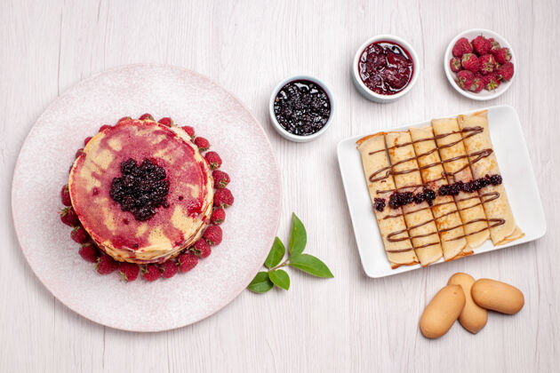 餐俯瞰美味的薄煎饼与草莓和果冻的白色办公桌派饼干甜水果蛋糕浆果草莓装饰早餐