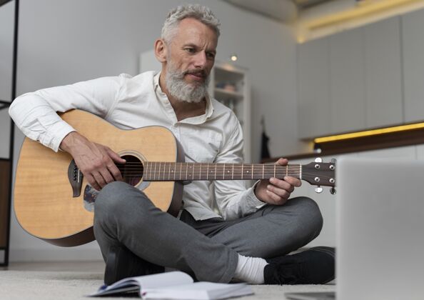 老年人大四的男人在家地板上学吉他议程家庭研究