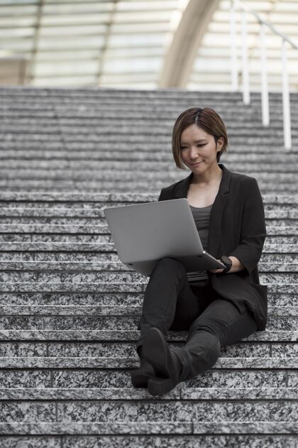 建筑坐在楼梯上拿着笔记本电脑的女人笔记本电脑设备现代