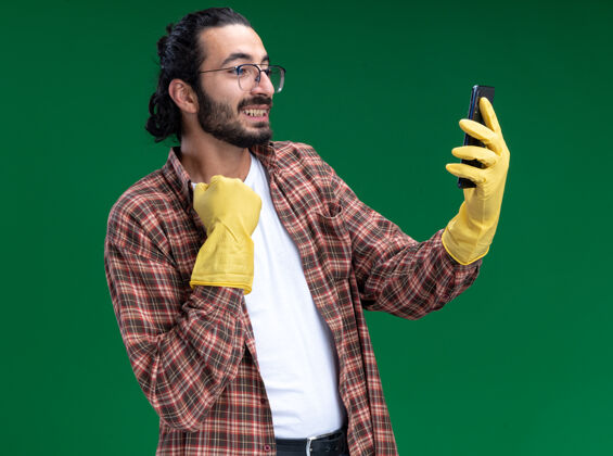 手套年轻帅气的清洁工穿着t恤 戴着手套 在绿色的墙上自拍 抓起衣领隔离人脸人