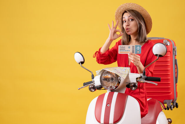 手提箱正面图身穿红色连衣裙的年轻女士拿着车票 在轻便摩托车上做着“ok”的手势轻便摩托车行李人