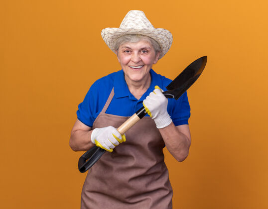 黑桃面带微笑的上了年纪的女园丁戴着园艺帽和手套拿着铲子拿着手套花园