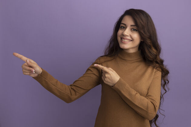 年轻微笑的年轻漂亮女孩穿着棕色高领毛衣点在一边孤立的紫色墙壁与复制空间脸感觉穿