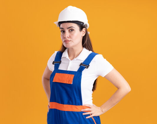 公民自信的穿着制服的年轻女建筑工人把手放在橘色的墙上衣服年轻人人