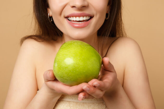 年轻特写黑发半裸完美皮肤的女人 裸妆把苹果隔离在米色粉彩墙上食物健身体重