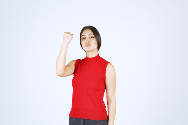 年轻穿红衬衫的女孩展示她的手臂肌肉和拳头强壮员工姿势