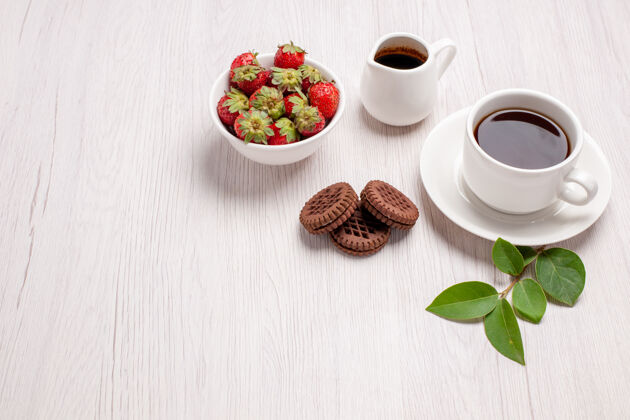 食物前视图一杯茶加巧克力饼干和草莓放在白桌子上糖茶饼干甜饼干糖茶杯子