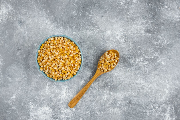 谷物一堆生玉米种子放在蓝色的碗里和木勺里勺子生的玉米