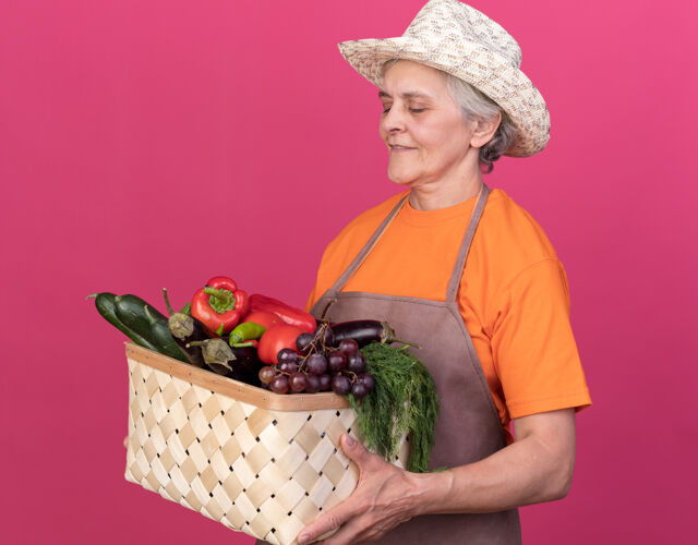 请高兴的上了年纪的女园丁戴着园艺帽捧着菜篮看着穿篮子帽子