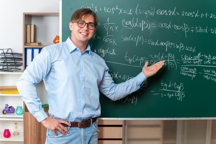 解释戴着眼镜的年轻男老师在教室里兴高采烈地微笑着站在黑板旁讲解数学公式年轻站穿