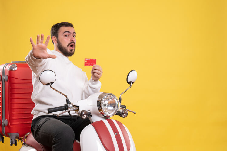 男人旅游旅游概念与年轻害怕旅行男子坐在摩托车上 手提箱上拿着黄色的银行卡运动摩托车年轻人