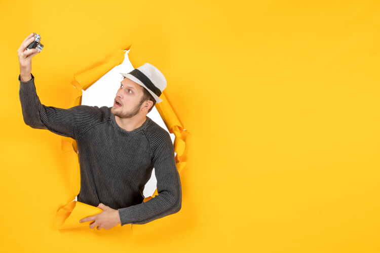 工作顶视图的年轻人拿着帽子 在一个撕破的黄色墙上看相机年轻人破建筑工