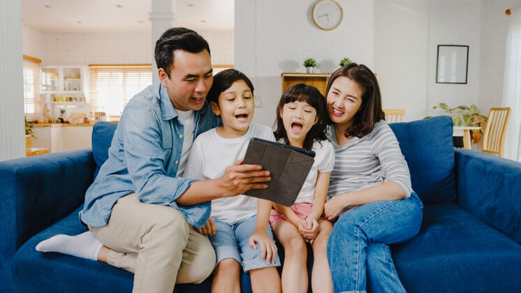 在一起快乐快乐的亚洲家庭爸爸 妈妈和孩子们在家里的沙发上玩得开心 使用数字平板电脑视频通话通信隔离男孩
