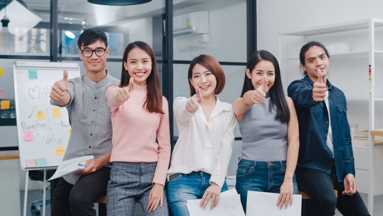 工作一群穿着时髦休闲装的亚洲年轻创意人士在创意办公场所微笑着竖起大拇指企业家办公室休闲