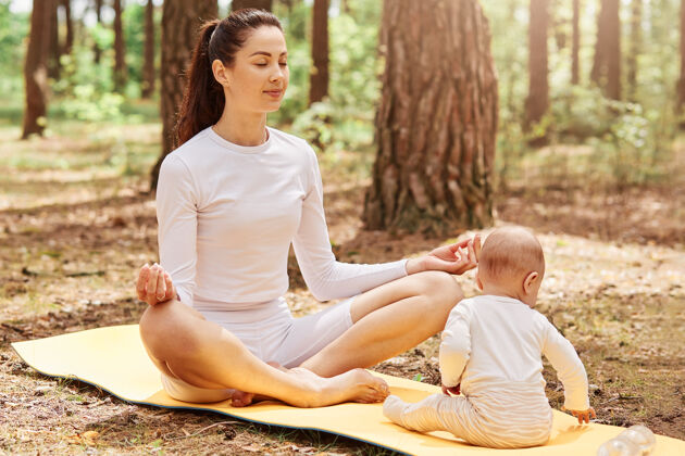 公园美丽的女人坐在莲花的姿势和冥想 而她的婴儿女儿画像快乐瑜伽爱