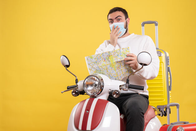 面具旅行的概念与惊讶的家伙在医疗面具坐在摩托车上 黄色的手提箱上 拿着黄色的地图摩托车黄色医疗