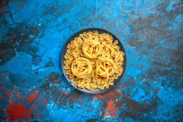 盘子在蓝色背景上的黑色盘子上用意大利面准备晚餐的俯视图传统洞阿拉伯