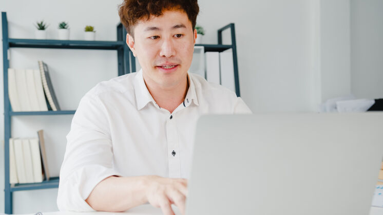 日语年轻的亚洲商人用笔记本电脑和同事谈论视频通话计划工作场所视频房子