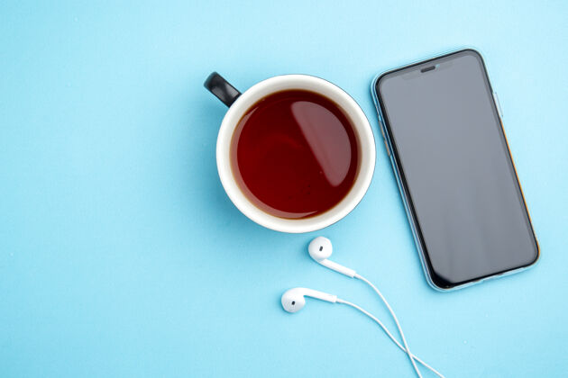背景蓝色背景上的一杯红茶手机耳机顶视图电话浓缩咖啡勺子