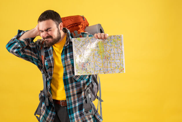 疼痛旅行概念与年轻的麻烦旅行的家伙背着背包拿着一张地图患有颈部疼痛的黄色男性黄色年轻人