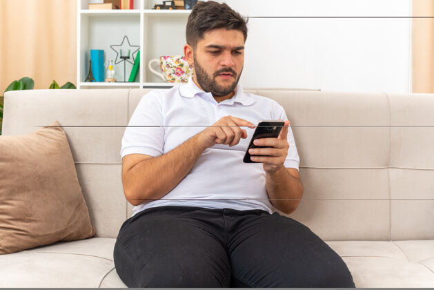 生活一个穿着休闲服的年轻人拿着智能手机输入各种信息 严肃地坐在客厅的沙发上看着屏幕年轻衣服手机