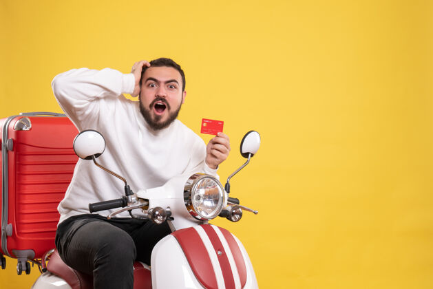 运动员旅游概念与年轻人惊讶的情绪旅行男子坐在摩托车上 手提箱上拿着黄色的银行卡运动摩托车人