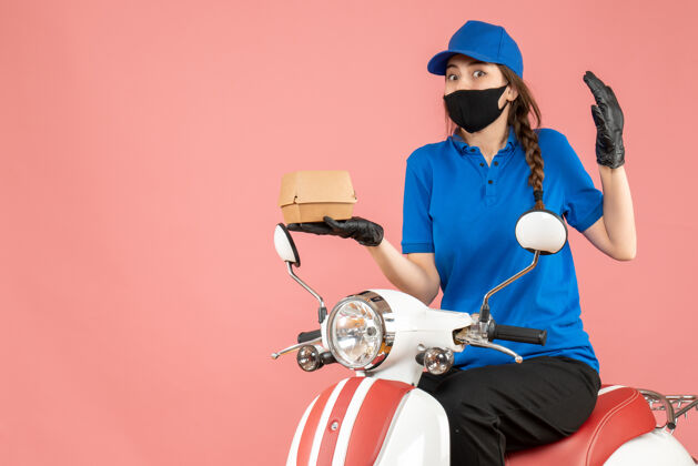摩托车俯视图惊讶的送货员戴着医用口罩和手套坐在滑板车上用粉彩桃子送订单送粉彩桃