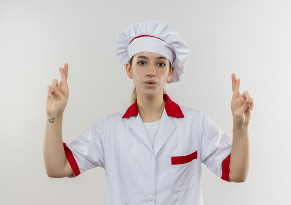 漂亮令人印象深刻的年轻漂亮厨师在厨师制服做交叉手指手势隔离在白墙上印象手指制服