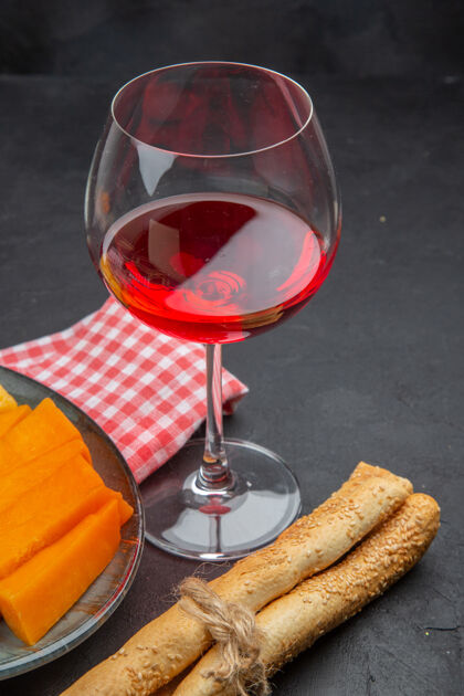 酒杯在一张黑色的桌子上 一杯美味的红酒和一条红色的毛巾上的切片奶酪的垂直视图葡萄酒切片酒精