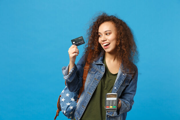 青少年年轻的非洲裔美国女孩十几岁的学生在牛仔服装 背包举行信用卡隔离在蓝色的墙上人货币奖励