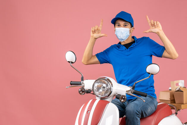 摩托车顶视图自信的快递员戴着医用面罩戴着帽子坐在滑板车上 在柔和的桃色背景下传递订单医疗订单桃