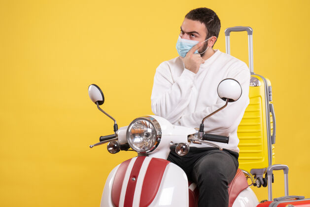 医疗旅行的概念和困惑的家伙在医疗面具坐在摩托车上 黄色的手提箱在它的黄色男性人物面具