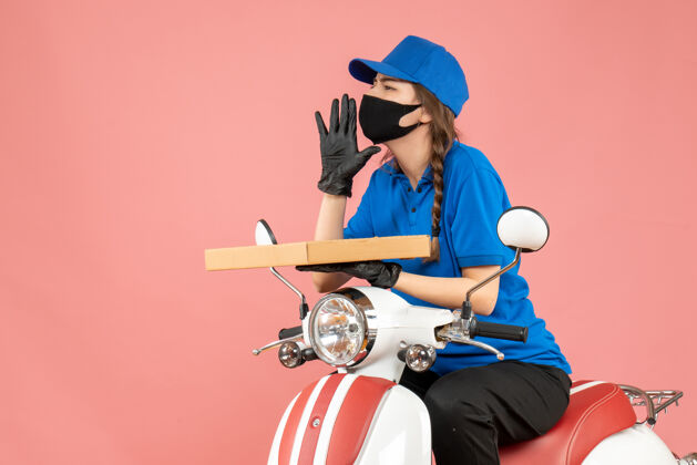 棒球手套俯视图：戴着医用面罩和手套的女快递员坐在滑板车上传递订单 在柔和的桃色背景下呼叫其他人人物桃子手套