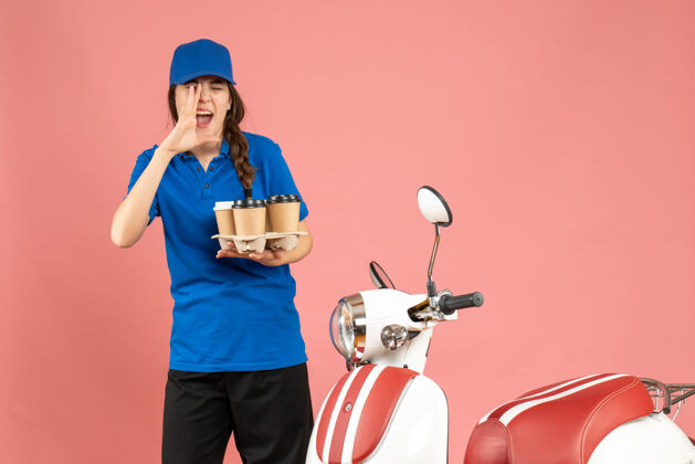 商务前视图快递女孩站在摩托车旁边拿着咖啡在粉彩桃色背景上呼唤某人咖啡人背景