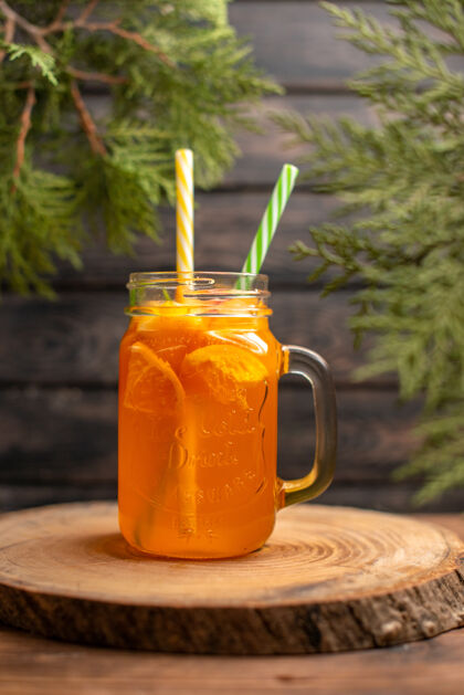 木材在棕色背景下 木制托盘上装有试管的玻璃杯中的新鲜橙汁的垂直视图管健康甜味剂