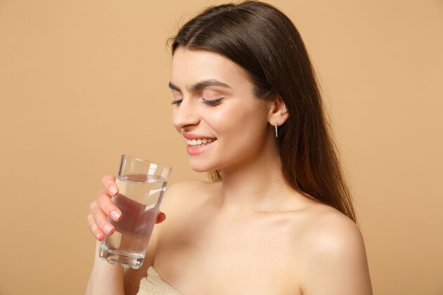 健康特写黑发半裸完美皮肤的女人裸妆玻璃水隔离米色粉彩墙饮食清洁感官