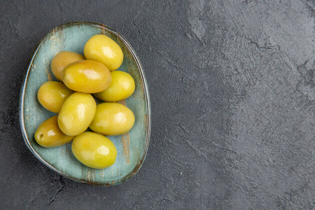 食品顶视图新鲜的有机绿色橄榄在一个蓝色的盘子在右侧的一个黑暗的背景健康盘子柠檬