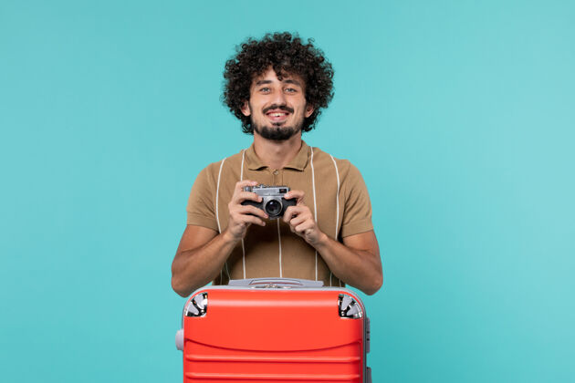 相机带着红色手提箱的度假男人用蓝色的相机拍照旅行包手提箱