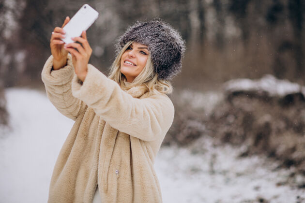 寒冷穿着冬衣的女人走在满是雪的公园里打电话电话户外自然