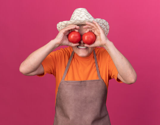 女未出租的上了年纪的女园丁戴着园艺帽 眼睛上覆盖着西红柿粉红色番茄不愉快