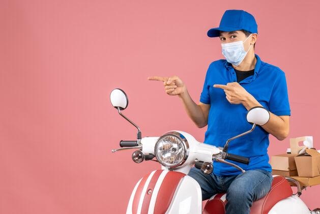 男顶视图的快递员戴着医疗面具戴着帽子坐在粉彩桃色背景上的踏板车上自行车摩托车摩托车