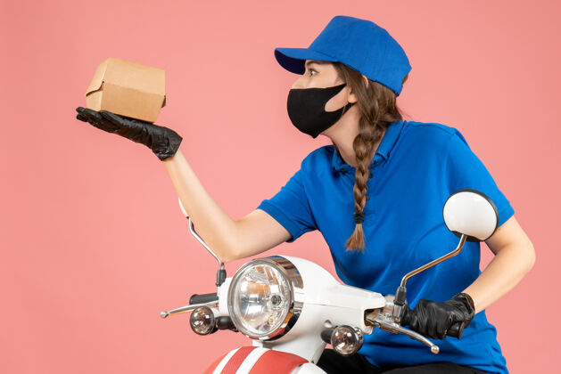 人俯视图为年轻集中女快递员戴着医用口罩和手套手持粉彩桃盒举行盒子面具
