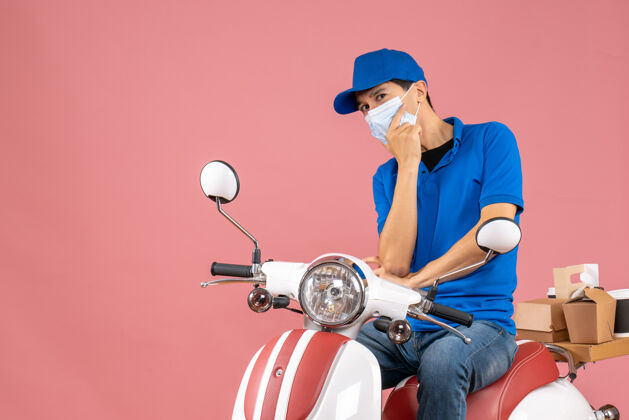 思考前视图思维快递员戴着医学面具戴着帽子坐在粉彩桃色背景的踏板车上桃面具摩托车