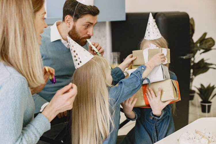 服装一家人和他们的两个女儿在厨房庆祝生日人们戴着派对帽女孩用盒子装礼物女人帽子衣服